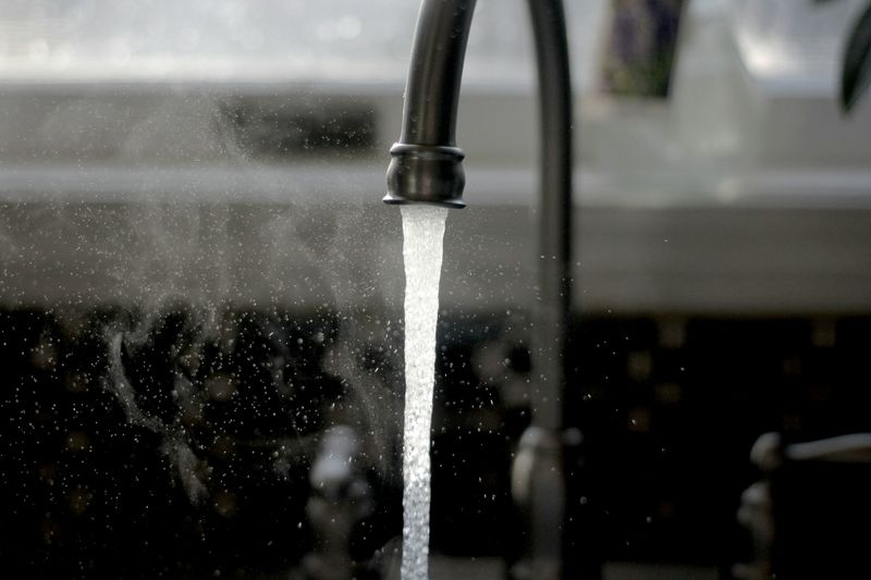 Hot water and steam running from a black kitchen faucet into a sink.